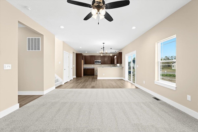 unfurnished living room featuring ceiling fan with notable chandelier and light carpet