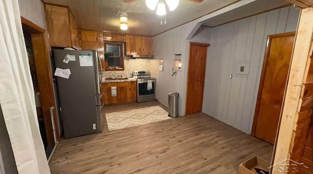 kitchen featuring wood walls, tasteful backsplash, light hardwood / wood-style flooring, ceiling fan, and stainless steel appliances