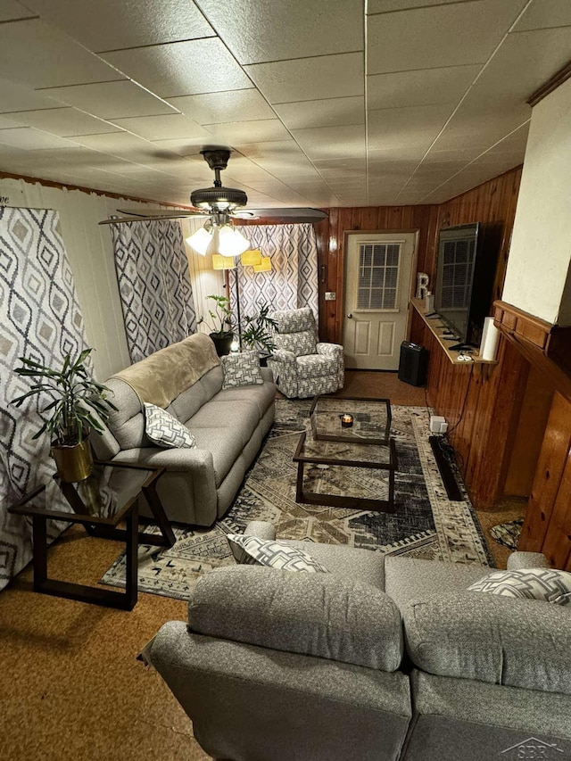 carpeted living area featuring a paneled ceiling, a ceiling fan, and wood walls