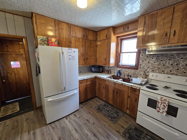 kitchen with light countertops, light wood-style flooring, a sink, white appliances, and under cabinet range hood