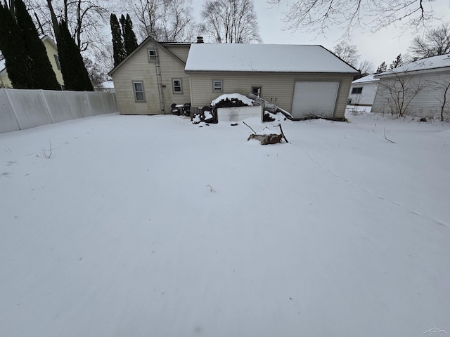 snow covered house with a garage, a chimney, and fence