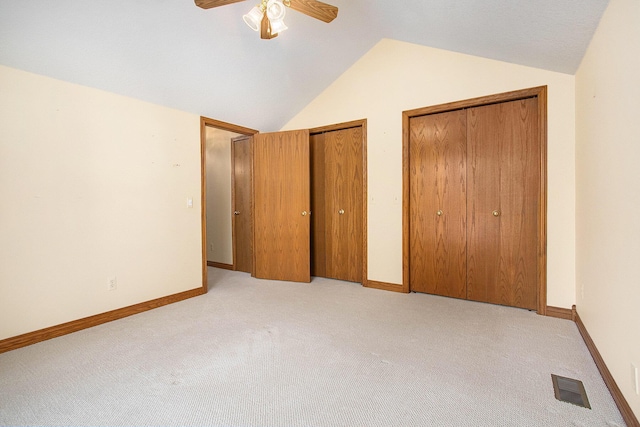 unfurnished bedroom featuring multiple closets, vaulted ceiling, light colored carpet, and ceiling fan