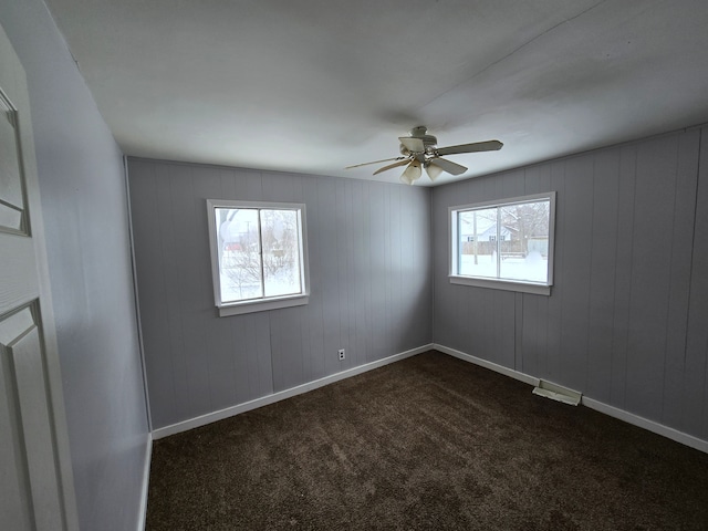 empty room featuring dark carpet, a ceiling fan, baseboards, and a healthy amount of sunlight
