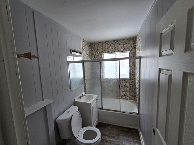 full bathroom featuring shower / bath combination with glass door, wooden walls, vanity, wood-type flooring, and toilet