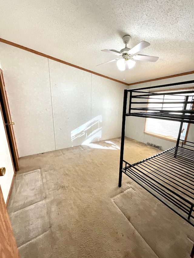 unfurnished bedroom featuring light carpet, a textured ceiling, crown molding, and ceiling fan