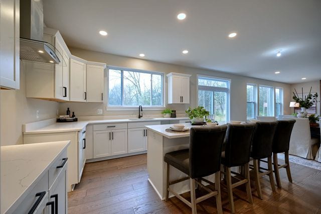 kitchen with wall chimney range hood, a breakfast bar, white cabinetry, dark hardwood / wood-style floors, and a kitchen island