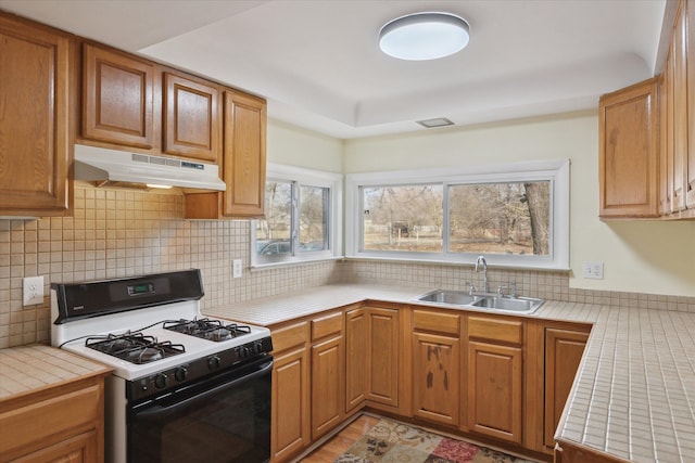 kitchen featuring gas range, tile countertops, sink, and backsplash