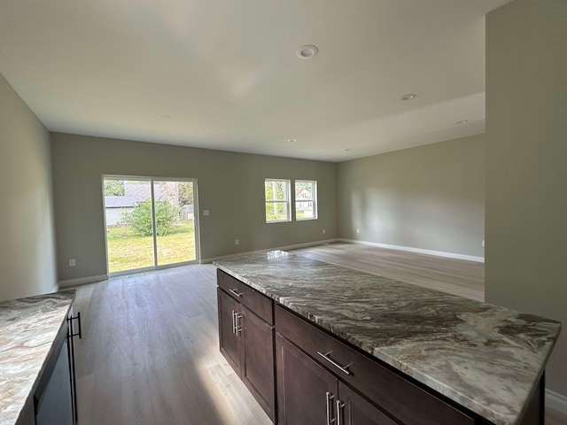 kitchen with dark brown cabinetry, a kitchen island, light stone counters, and light hardwood / wood-style floors