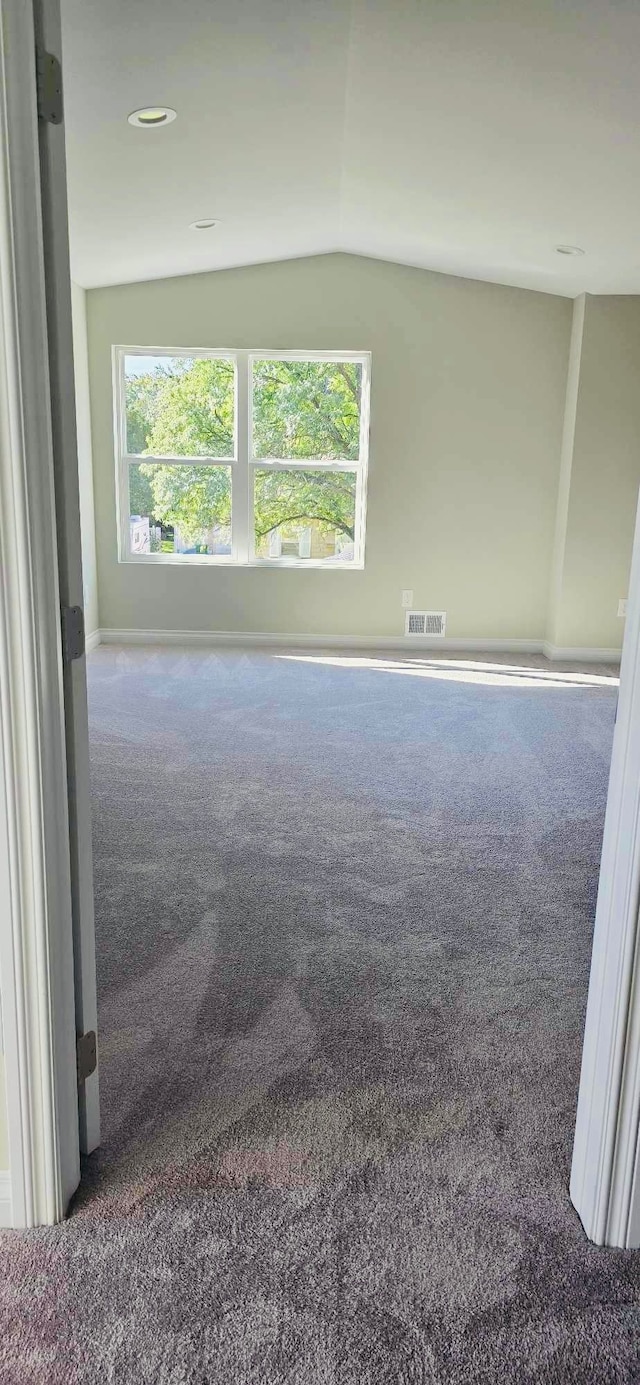 spare room featuring lofted ceiling, dark carpet, and a wealth of natural light