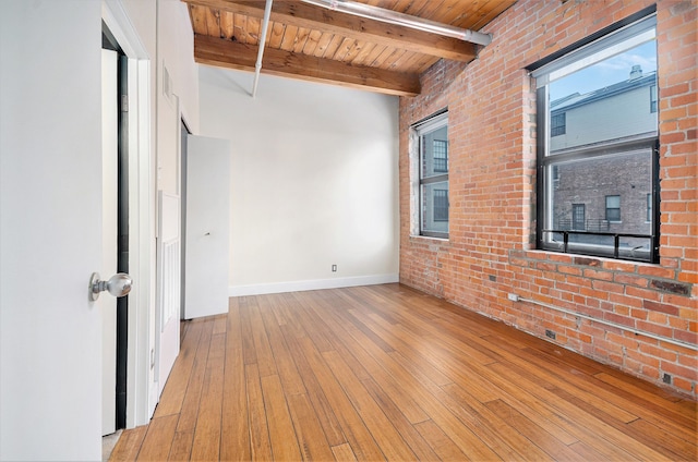 empty room featuring beam ceiling, brick wall, wooden ceiling, and light wood-type flooring