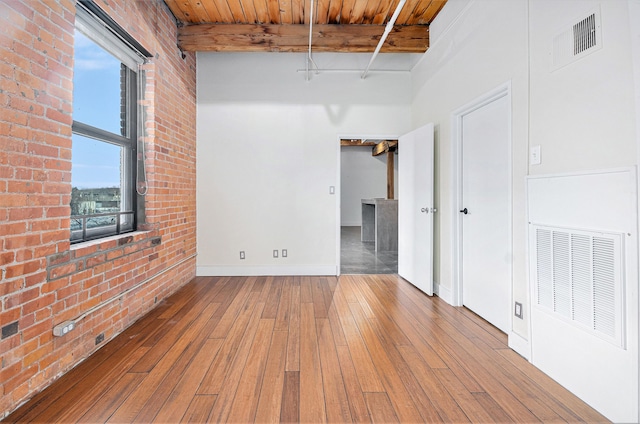 empty room with wood-type flooring, brick wall, wooden ceiling, and beam ceiling