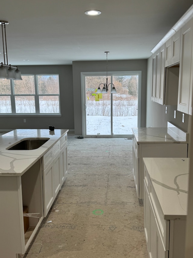 kitchen featuring pendant lighting, white cabinets, a center island, light stone counters, and an inviting chandelier