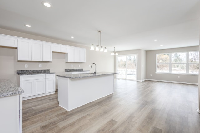 kitchen with light wood finished floors, white cabinets, light stone countertops, a sink, and recessed lighting