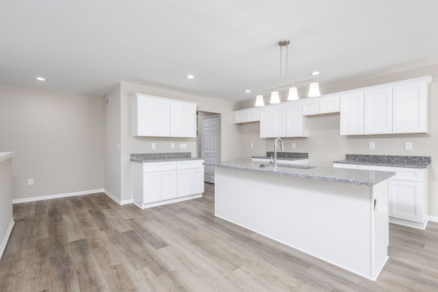 kitchen with recessed lighting, white cabinets, a sink, an island with sink, and light wood-type flooring