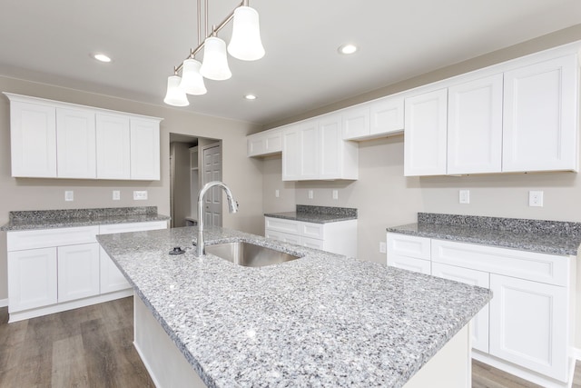 kitchen with light stone counters, dark wood-style flooring, a center island with sink, recessed lighting, and a sink