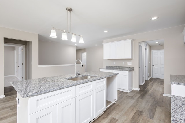 kitchen with recessed lighting, white cabinets, a sink, light stone countertops, and light wood-type flooring