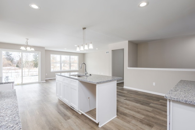 kitchen with baseboards, wood finished floors, white cabinetry, a sink, and recessed lighting