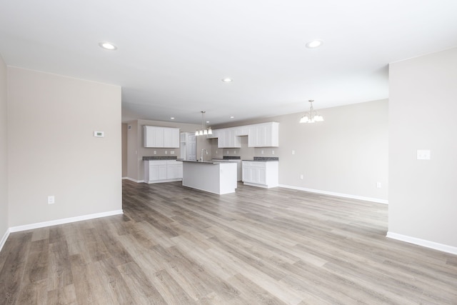 unfurnished living room featuring recessed lighting, baseboards, a notable chandelier, and light wood finished floors