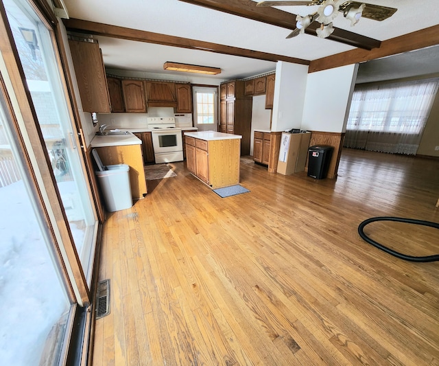 kitchen with a center island, white range with electric cooktop, light countertops, beam ceiling, and light wood-style flooring