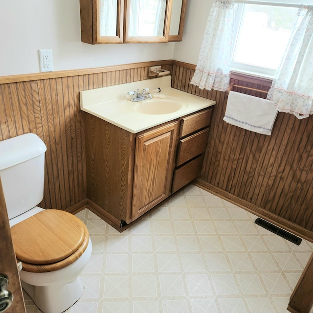 half bath featuring tile patterned floors, a wainscoted wall, visible vents, toilet, and wood walls