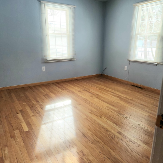 unfurnished room with baseboards, plenty of natural light, light wood-style floors, and visible vents