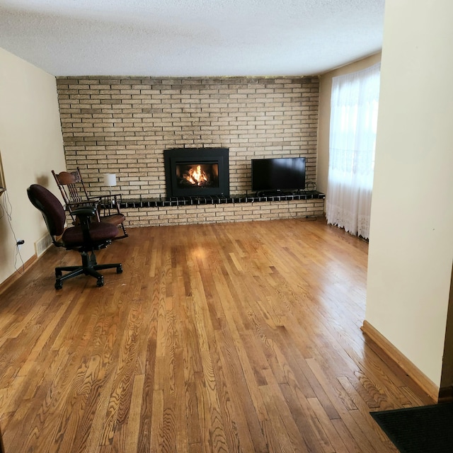 unfurnished living room with visible vents, a brick fireplace, a textured ceiling, and wood finished floors