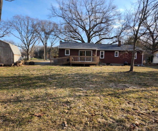 rear view of house featuring a lawn, a deck, a chimney, and an outdoor structure