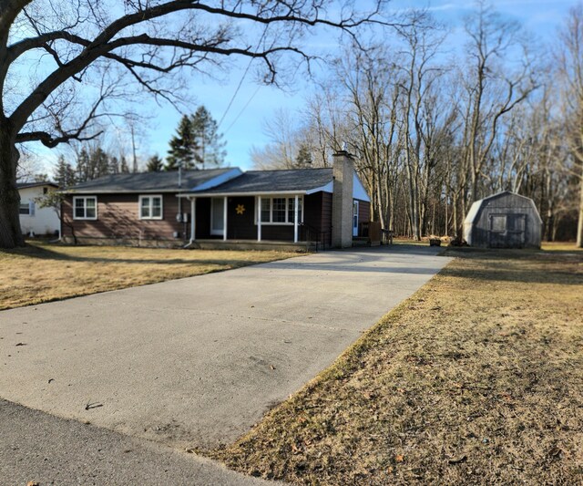 ranch-style home featuring a front yard, driveway, covered porch, a chimney, and an outdoor structure