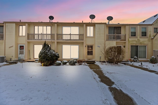 snow covered house featuring central AC unit and a balcony