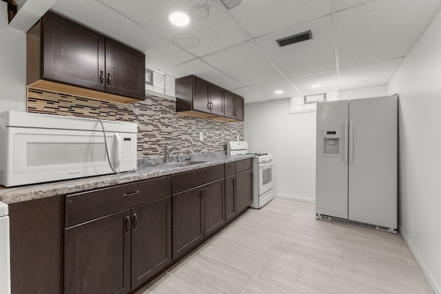 kitchen with white appliances, sink, dark brown cabinets, and backsplash