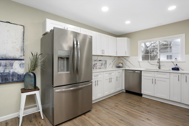 kitchen featuring sink, light hardwood / wood-style flooring, white cabinetry, backsplash, and stainless steel appliances