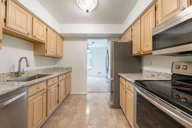 kitchen with sink, stainless steel appliances, light stone countertops, light brown cabinetry, and light colored carpet