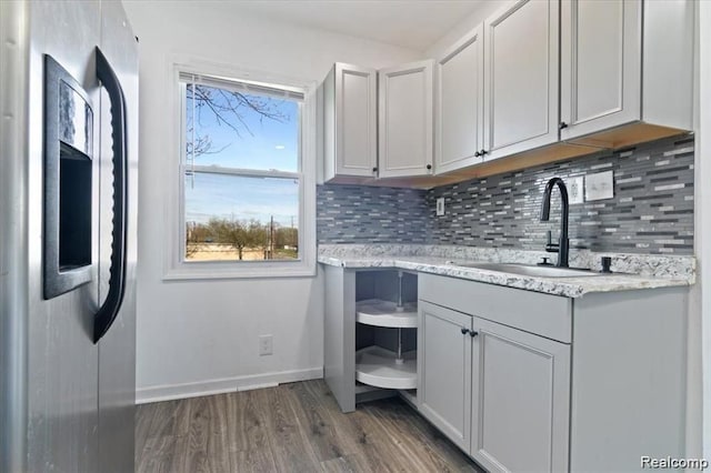 kitchen featuring sink, dark wood-type flooring, light stone counters, stainless steel fridge with ice dispenser, and decorative backsplash