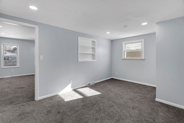 spare room featuring a healthy amount of sunlight, dark carpet, and built in shelves