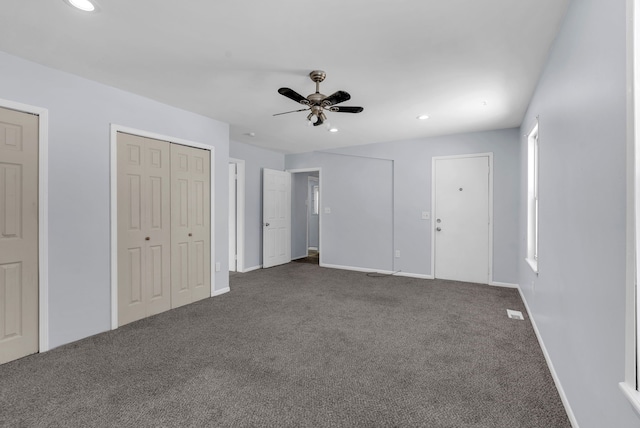 unfurnished bedroom with ceiling fan, two closets, and dark colored carpet