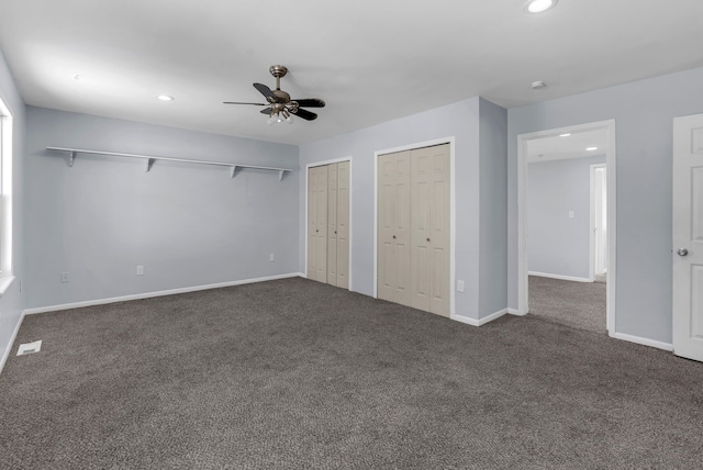 unfurnished bedroom featuring dark colored carpet, two closets, and ceiling fan