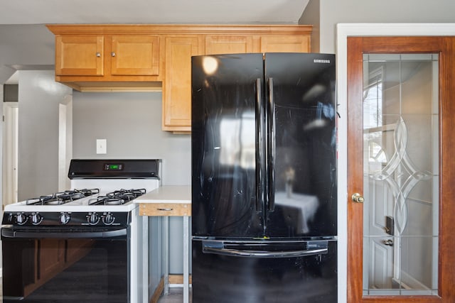 kitchen with gas stove, black fridge, and light brown cabinetry