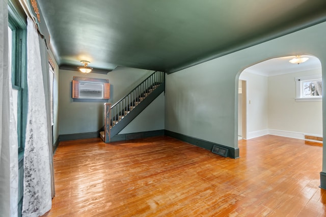 626 Orange St, Jackson, MI 49202 - unfurnished living room with arched walkways, hardwood / wood-style floors, stairs, baseboards, and a wall mounted air conditioner