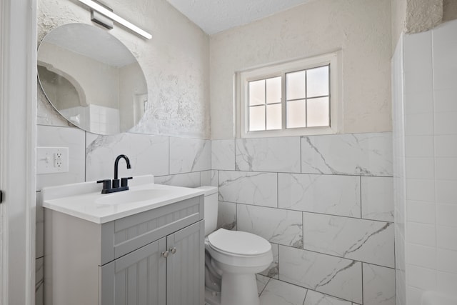 bathroom featuring vanity, toilet, a textured ceiling, and tile walls