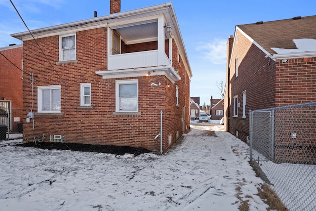 snow covered back of property featuring a balcony