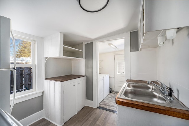 kitchen featuring washing machine and clothes dryer, lofted ceiling, sink, hardwood / wood-style floors, and white cabinets