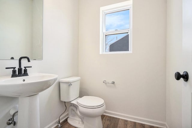 half bath featuring toilet, a sink, baseboards, and wood finished floors