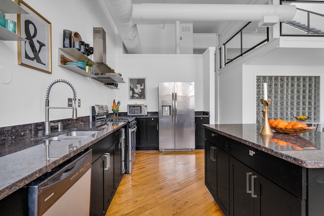 kitchen with light wood-type flooring, appliances with stainless steel finishes, sink, and dark stone countertops