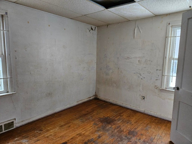 spare room with dark wood-type flooring, a wealth of natural light, and a drop ceiling