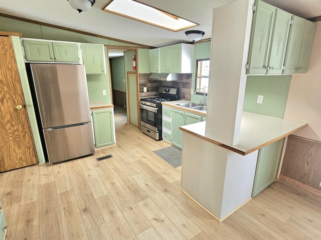 kitchen with appliances with stainless steel finishes, sink, vaulted ceiling with skylight, and light hardwood / wood-style floors