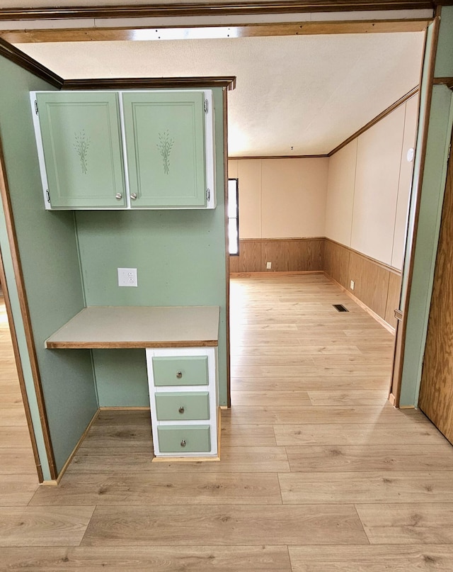 unfurnished office featuring ornamental molding, wooden walls, built in desk, and light hardwood / wood-style floors