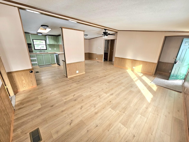 unfurnished living room featuring sink, ceiling fan, wooden walls, a textured ceiling, and light wood-type flooring