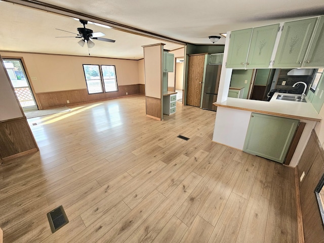 kitchen with green cabinetry, stainless steel fridge, kitchen peninsula, and sink