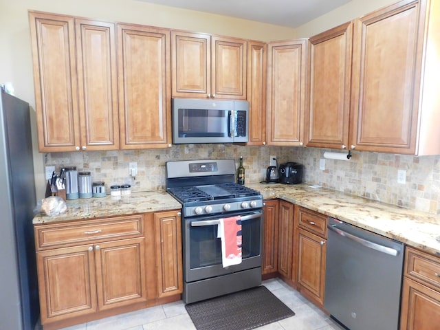 kitchen featuring light tile patterned flooring, appliances with stainless steel finishes, light stone counters, and backsplash