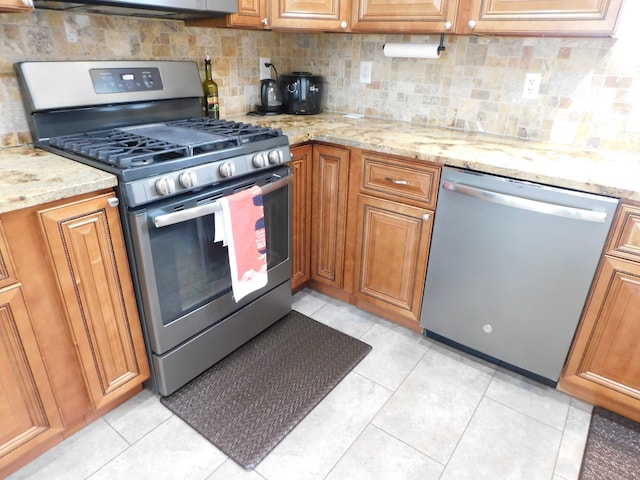 kitchen featuring light tile patterned floors, decorative backsplash, stainless steel appliances, and light stone countertops